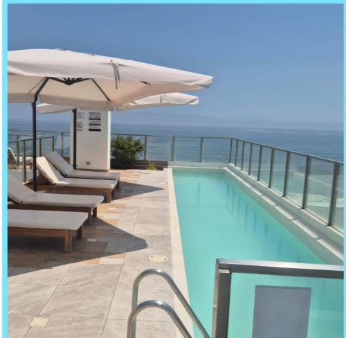 uma piscina com guarda-sol e cadeiras e o oceano em Departamento frente al mar costa verde em Lima