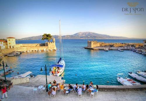 a group of people sitting at tables in a harbor with a boat at Spon Boutique Hotel in Nafpaktos