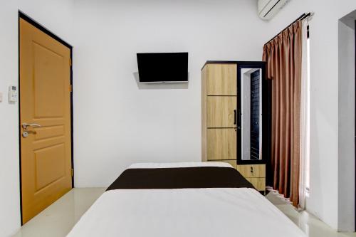 ein Schlafzimmer mit einem weißen Bett und einem Fernseher in der Unterkunft Hotel O Rumah Daun Guesthouse Jogja in Demangan