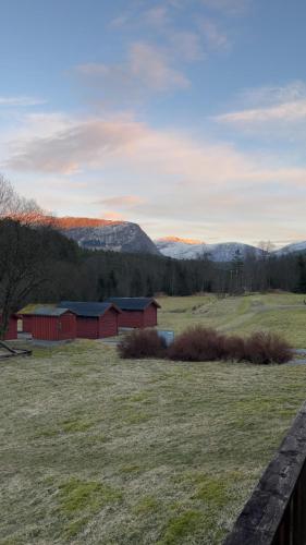 a red barn in a field with mountains in the background at Døskelandslia Camping in Sygna