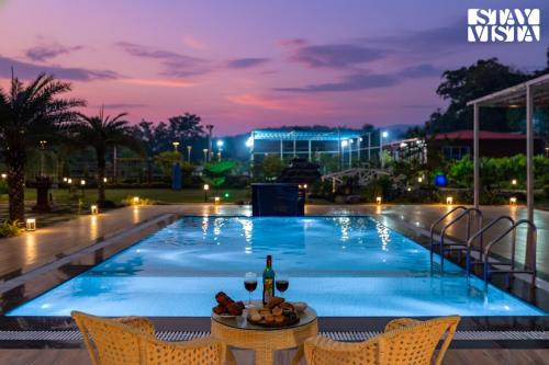 a pool at night with a table with wine glasses at StayVista at The Red Creek with BBQ and Bonfire in Nagothna