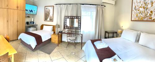 una habitación de hotel con dos camas y un escritorio en Clubview Guest House, en Centurion