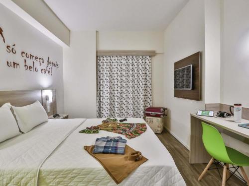 um quarto com uma cama, uma secretária e uma cadeira verde em ibis Styles Vitoria da Conquista em Vitória da Conquista