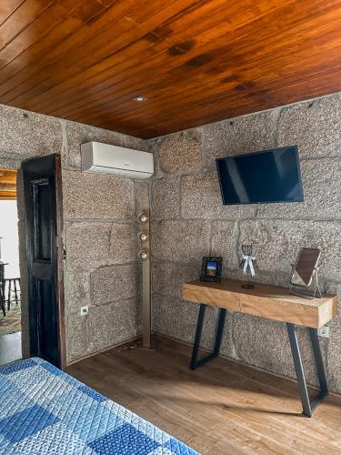 a room with a table with a tv on a stone wall at Casa do Cabeço de Boi by Refúgio ao Luar in Terras de Bouro