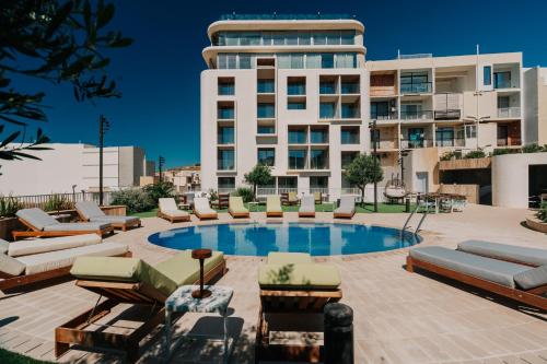 ein Schwimmbad mit Liegestühlen und ein Gebäude in der Unterkunft Reef Hotel & Spa in Marsalforn
