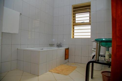 a white tiled bathroom with a tub and a window at Calm Suites Kampala in Kampala