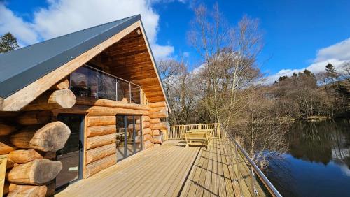 eine Blockhütte mit einer Holzterrasse neben einem See in der Unterkunft Kingfisher Cabin in Broughton in Furness