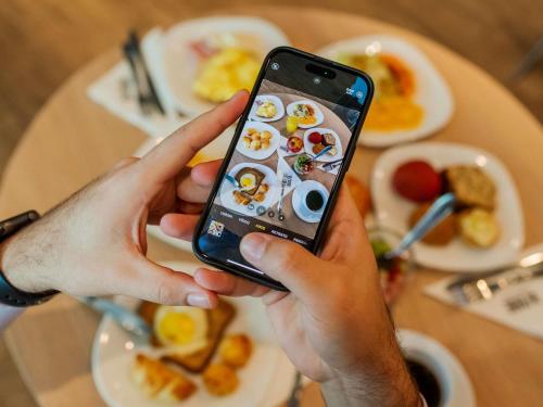 a person holding a cell phone in front of a table of food at ibis Porto Alegre Moinhos de Vento in Porto Alegre