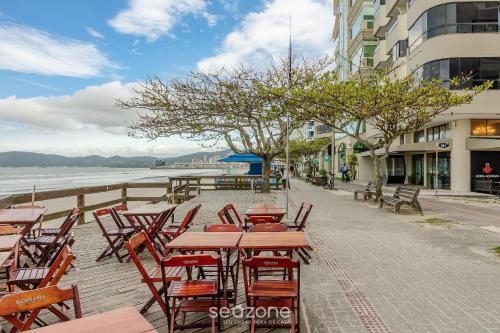 uma fileira de mesas e cadeiras em uma calçada perto da água em Aptos em Prédio à Beira-mar em Meia Praia, Itapema - EVBs em Itapema