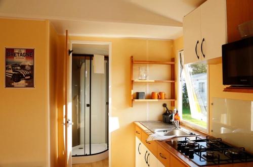 a kitchen with a sink and a stove in it at Mobil-home Les volets rouges in Plouhinec