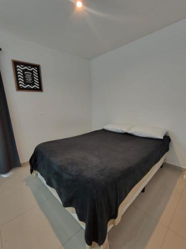 Cama en habitación blanca con manta negra en Centrico loft, en Puerto Madryn