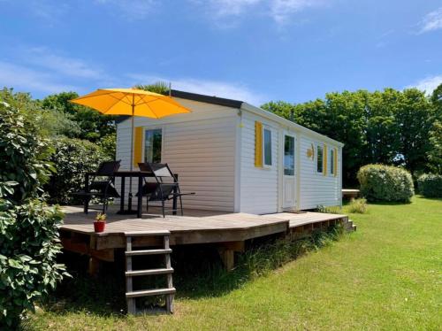a tiny house with a table and an umbrella at Mobil-home Les volets jaunes in Plouhinec