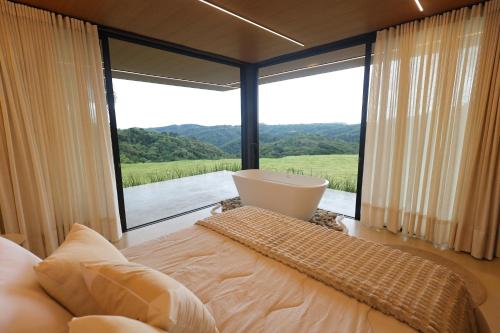 a bedroom with a large window with a bed and a tub at Casa de Campo - Valle Paixão in Campo Largo
