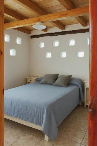 a bedroom with a bed with blue sheets and wooden ceilings at Cabañas LuCes del Pirque in El Hoyo