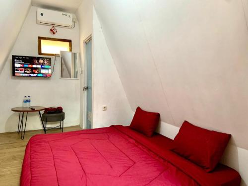 Sokkyo Homestay Kaliurang في Ngemplak: سرير احمر في غرفة بيضاء مع طاولة