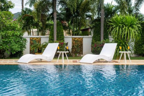 a pool with white chairs and tables next to a house at Villa with Huge Private Pool and Tropical Garden Just 10 Minutes Walk to Kamala Beach in Kamala Beach