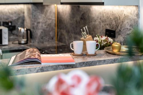 a counter with two coffee cups and a book on it at Stylish 1BR Apartment at Damac Hills Golf Gate in Dubai