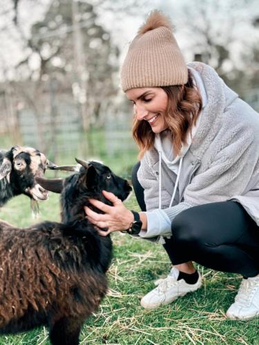 a woman is petting two goats in a field at Historic Farm Romance with Miniature Goat Feeding at Hideaway Farmlet in Penguin