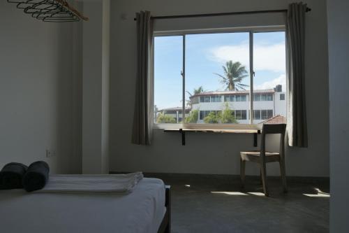 a room with a bed and a desk and a window at The Stables Oceanfront Hotel Midigama in Midigama East