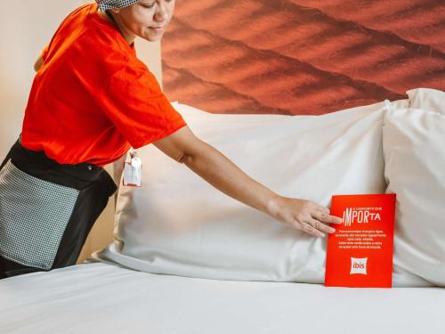 um homem de camisa laranja arrumando uma cama em ibis Juazeiro do Norte em Juazeiro do Norte