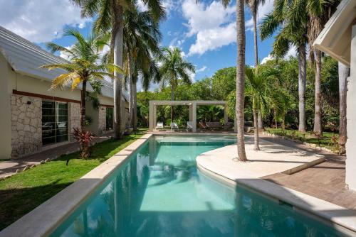 a swimming pool with palm trees and a house at Casa Vela - 2BR - Where Waves Meet Relaxation in Cancún