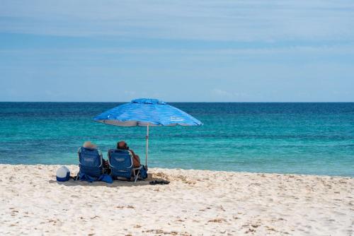 two people sitting in chairs under an umbrella on the beach at Casa Marea - 2BR - Tropical Vibes & Palm Breeze Oasis in Cancún