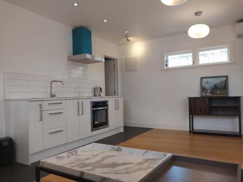 a kitchen with white cabinets and a sink and a table at Oranga Comfort Stay in Auckland