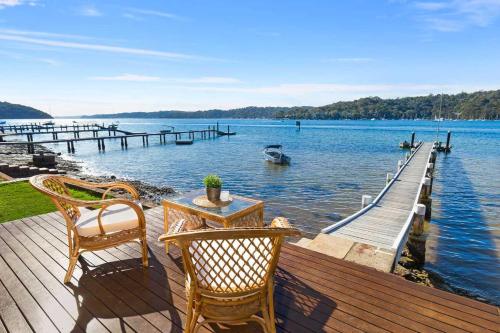 a wooden dock with two chairs and a table on the water at Waterfront Scotland Island Holiday Home - Family & Pet Friendly - 3 Bedrooms - Wifi - Netflix - Private Jetty in Scotland Island