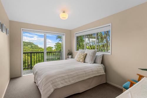 Waipu CoveTreetop Break - Waipu Cove Holiday Home的一间卧室设有一张床和两个大窗户
