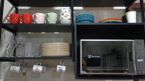 a cabinet with plates and cups and a microwave at Espaço Isha Canelinha in Canelinha