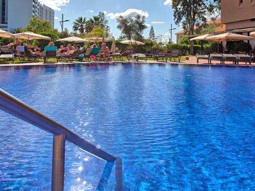 a large blue swimming pool with people sitting in chairs at Dom Pedro Marina in Vilamoura