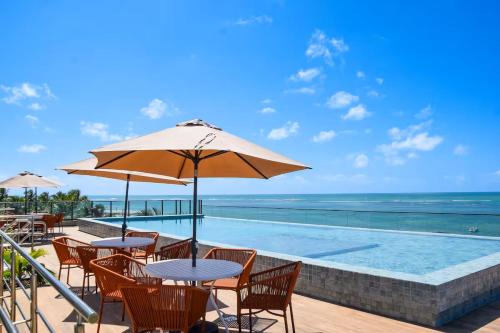 una piscina con tavoli, sedie e un ombrellone di FLAT Beira Mar Tamandare a Tamandaré