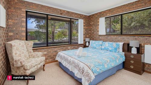 a bedroom with a bed and a chair and windows at Cuttagee Beach Cottage 3 - Tathra Bermagui Rd 3521 in Barragga Bay