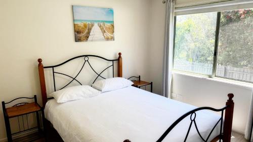 a bedroom with a bed with white sheets and a window at Tanjil Cottage in Lakes Entrance