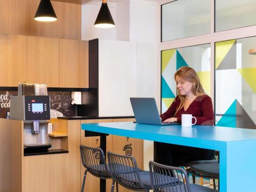 a woman sitting at a blue table with a laptop at Aparthotel Adagio Access Paris Vanves - Porte de Versailles in Vanves
