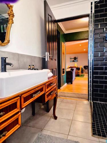 a bathroom with a large white sink and a living room at The Green Door Cottage in Roodepoort