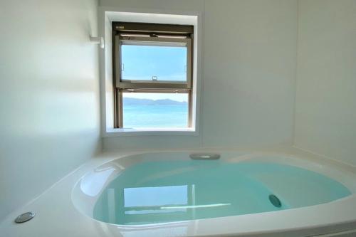a bath tub in a white room with a window at isola villa amami in Tatsugo