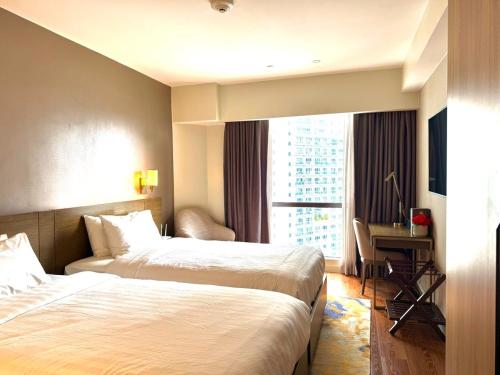 a hotel room with two beds and a desk and a window at Mesmerizing Twin Bed with Rockwell View in Manila