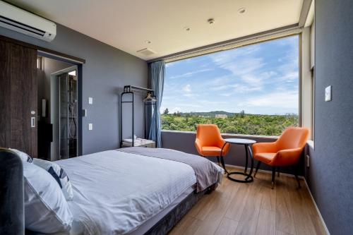 1 dormitorio con 1 cama, 2 sillas y una ventana grande en Ocean Villa Fuchaku Okinawa, en Fuzuchi
