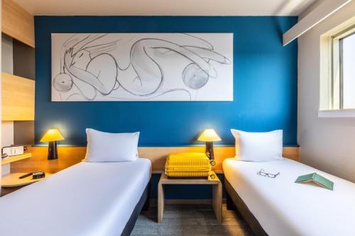 duas camas em um quarto com uma parede azul em ibis Paris Porte de Montreuil em Paris