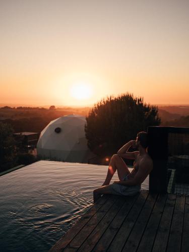 a man sitting on the edge of a swimming pool at wecamp Reserva Alecrim in Santiago do Cacém