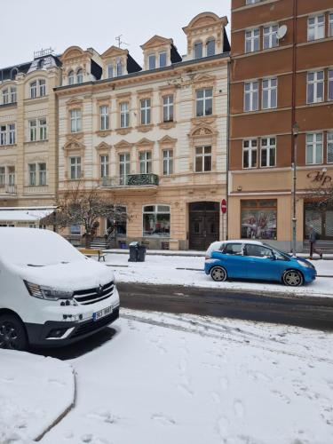 una macchina blu parcheggiata di fronte a un edificio nella neve di Apartment Natali a Karlovy Vary