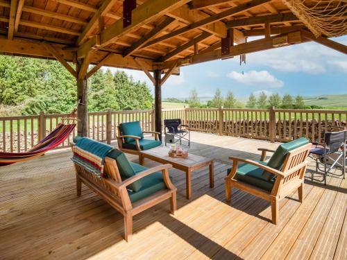 een terras met stoelen en een hangmat op een houten dek bij Broomstick Cottage in Elsdon