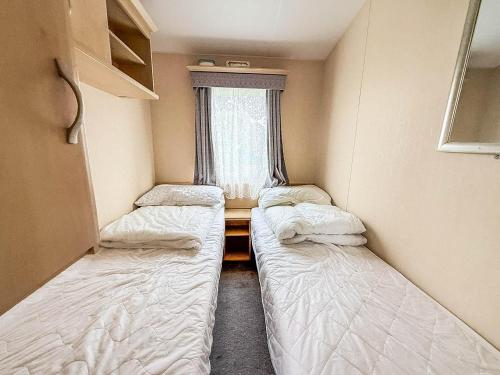 zwei Betten in einem kleinen Zimmer mit Fenster in der Unterkunft 6 Berth Caravan With Decking At Naze Marine Holiday Park Ref 17071P in Walton-on-the-Naze