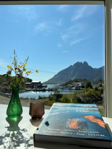 a book and a vase on a table with a window at Aurora Bay Villa Lofoten 罗弗敦极光湾海景顶层别墅 in Sund