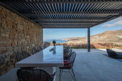 a table and chairs on a patio with a stone wall at Aora Villa Ftelia Beach Mykonos in Panormos Mykonos