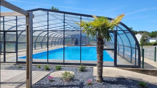 Un invernadero con una palmera frente a una piscina. en Chalet dans résidence privée avec piscine couverte, en Marzan