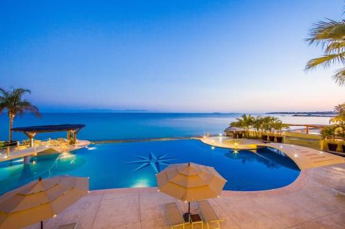 a swimming pool with umbrellas and the ocean at Luxury Oceanfront Condo Infinity Pool in Punta Mita