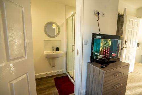 Queens Court Ensuite Studio في ستوك أون ترينت: حمام فيه تلفزيون على دولاب مع مغسلة