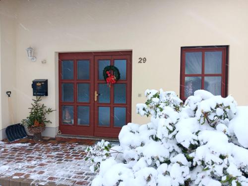 a snow covered tree in front of a red door at Ferienhaus Töpferblick-Hartau in Hartau